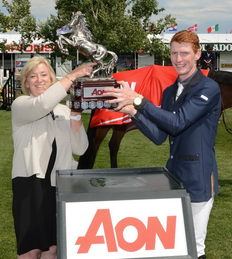 Daniel Coyle hoists the Champions trophy with Christine Lithgow, President & CEO, AON. Photo (c) Spruce Meadows Media Services.