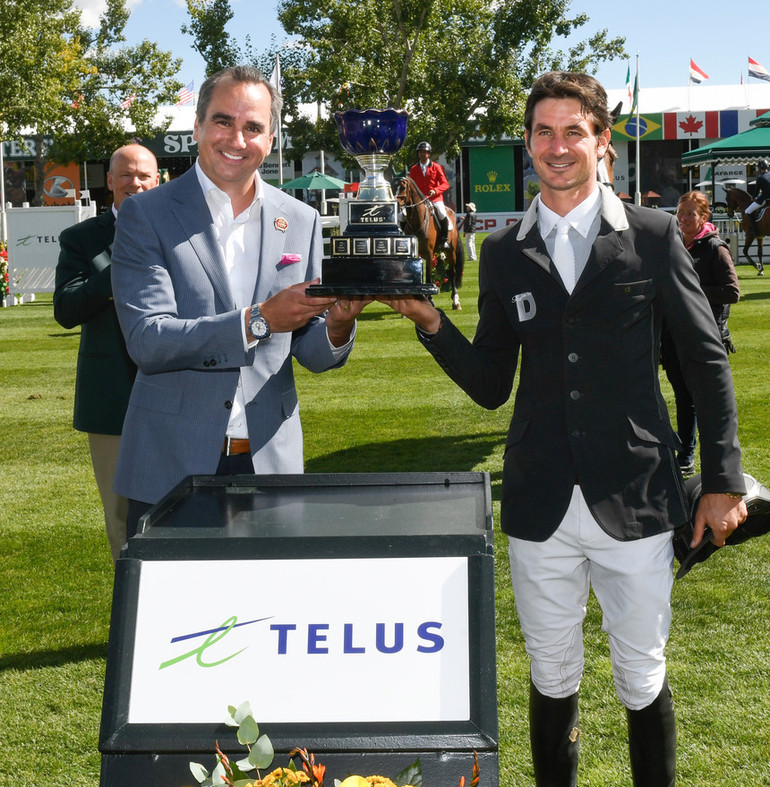 Steve Guerdat (SUI) hoist the champions trophy with Lorenzo DeCicco, Vice President, TELUS Business Solutions. Photo (c) Spruce Meadows Media Services. 
